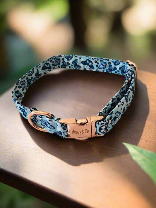 Honey's Butterfly Dog Collar by Honey & Co, featuring a blue butterfly design with a rose gold buckle, displayed on a wooden surface.